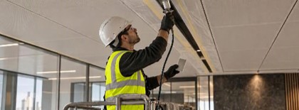 Operative on a mobile platform spraying a colour-matched finish onto a ceiling service channel